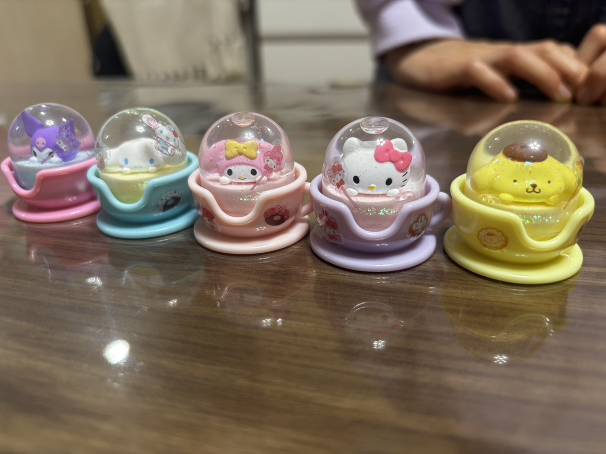 ティーカップ型のミニチュアマスコット5個(クロミ、シナモロール、マイメロディ、ハローキティ、ポムポムプリン)が机の上に並んでいる写真