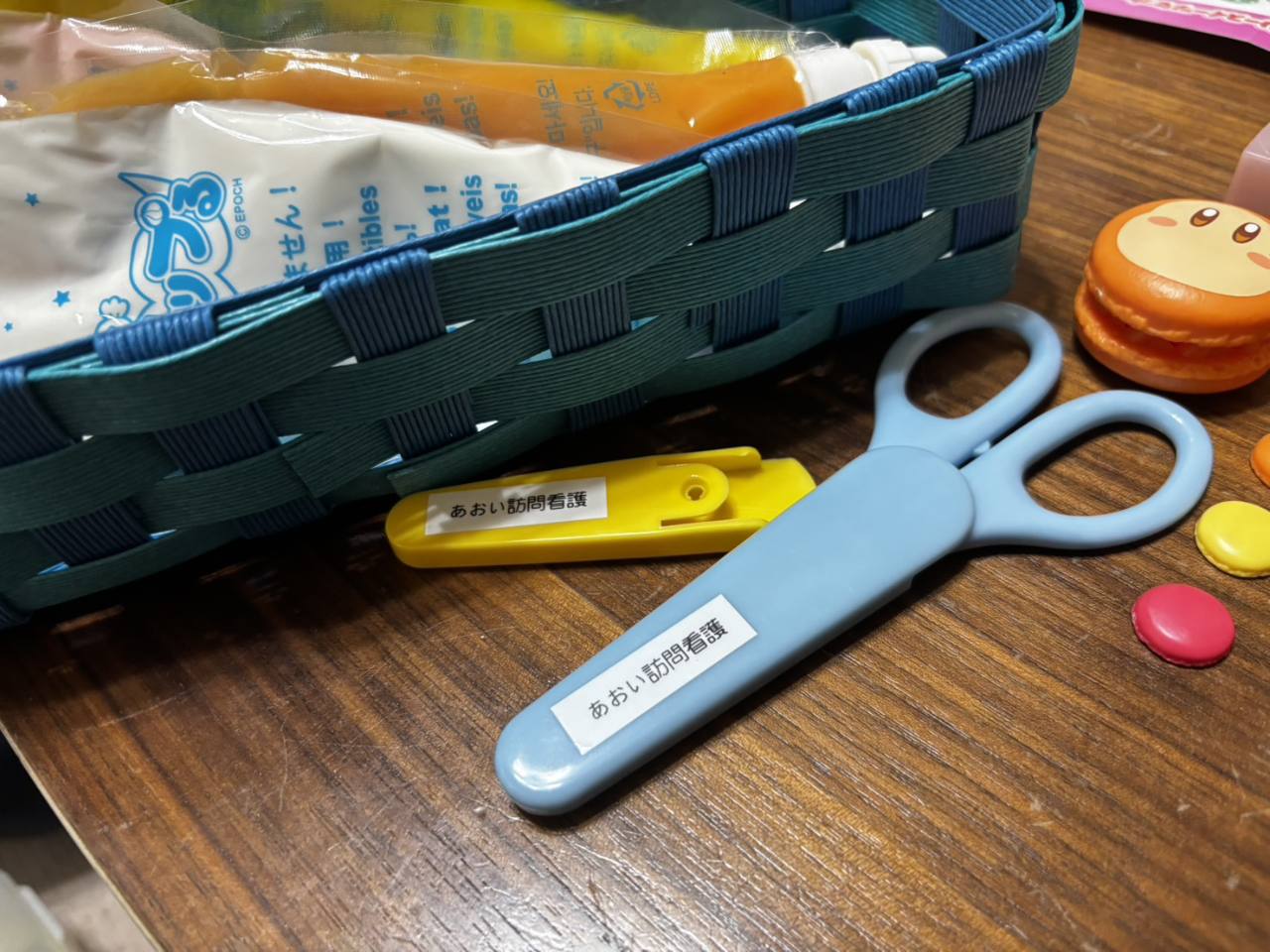 青い紙バンドのかごと、あおい訪問看護のラベルを付けたはさみなどの道具