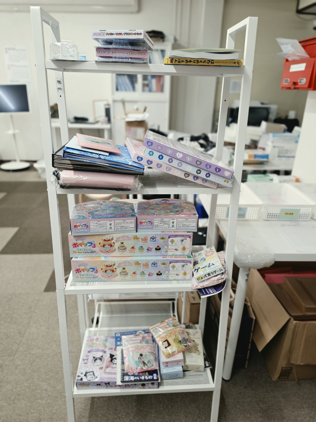 白いラックに並んだ子ども向けの工作キット、ぬりえ、絵本、カードゲーム