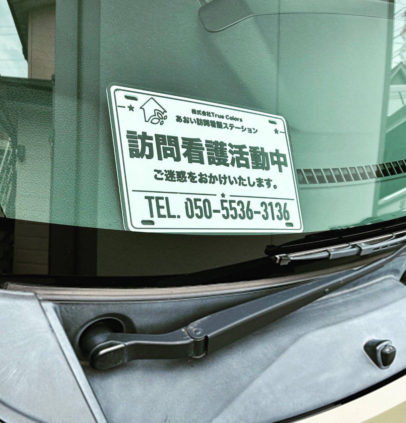 車のフロントガラスの内側に置かれた、「訪問看護活動中」と事業所名・電話番号が入った白いプレートの写真