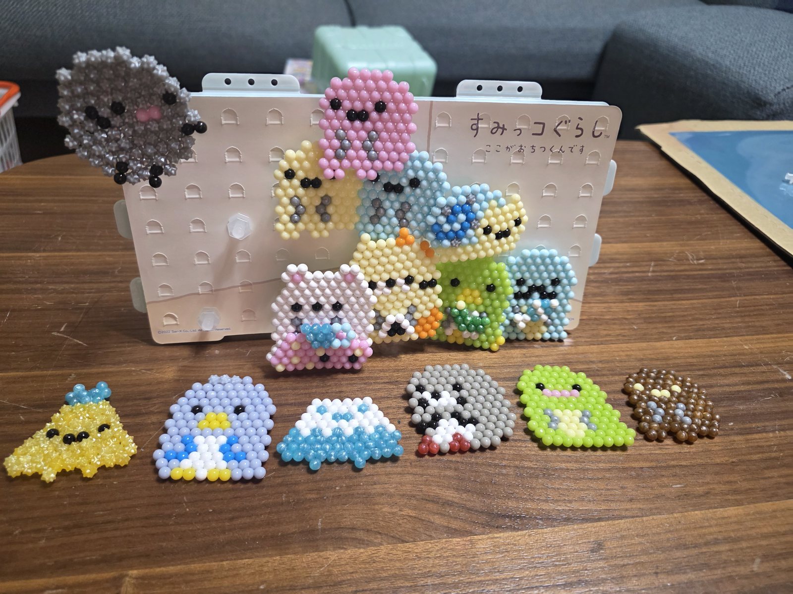 小さなビーズを並べて作ったキャラクターの作品15点。立てた台に9点、手前の机に6点が並んでいる