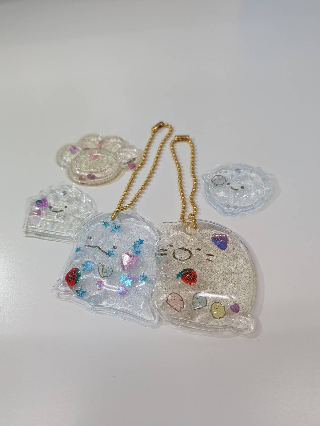 星やハート、いちごのパーツが入った透明なキーホルダーと、金色のボールチェーン。ほかに型から外した作品が3つ並ぶ