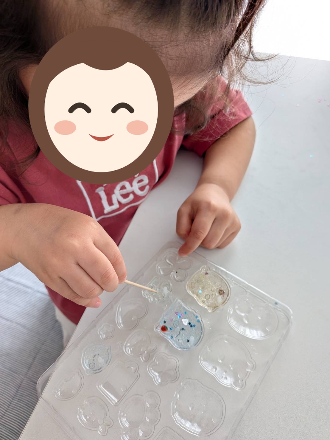 お子さんがつまようじの先で、透明な型の中のパーツの位置を直している写真。もう片方の指で型を押さえている