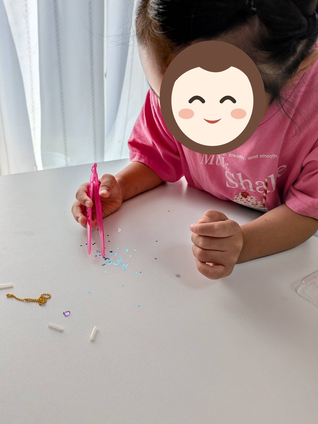 お子さんがピンク色のピンセットで、机に広げた小さな星形のパーツをつまんでいる写真