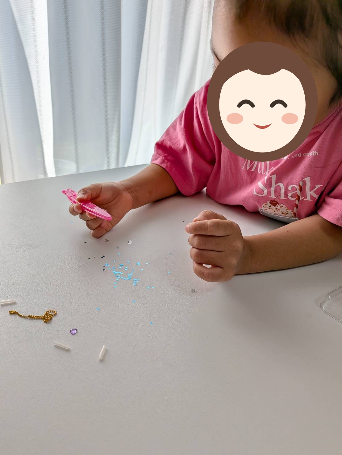 ピンセットを持ち直し、つまんだパーツを見ているお子さんの写真。机にはボールチェーンや小さなパーツが並ぶ