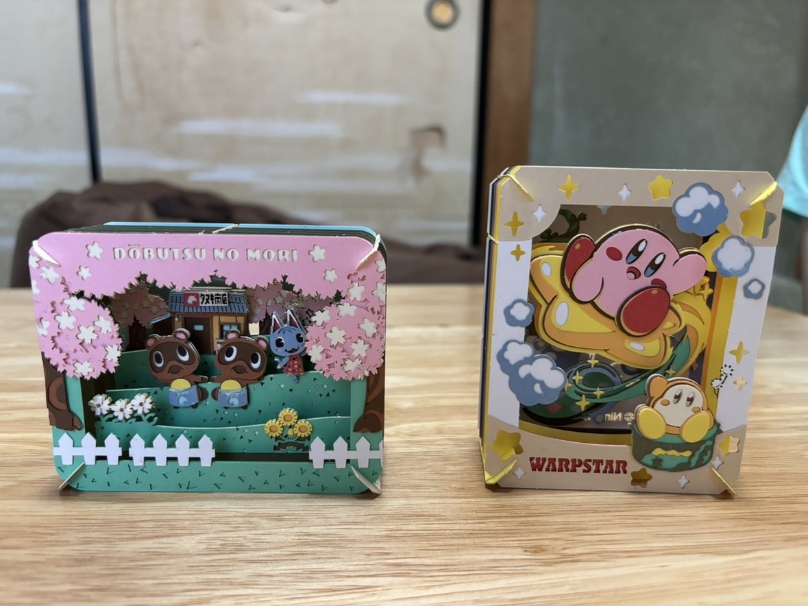 組み立てたペーパーシアター2点。桜の下に動物のキャラクターが並ぶ場面と、星に乗ったキャラクターの場面